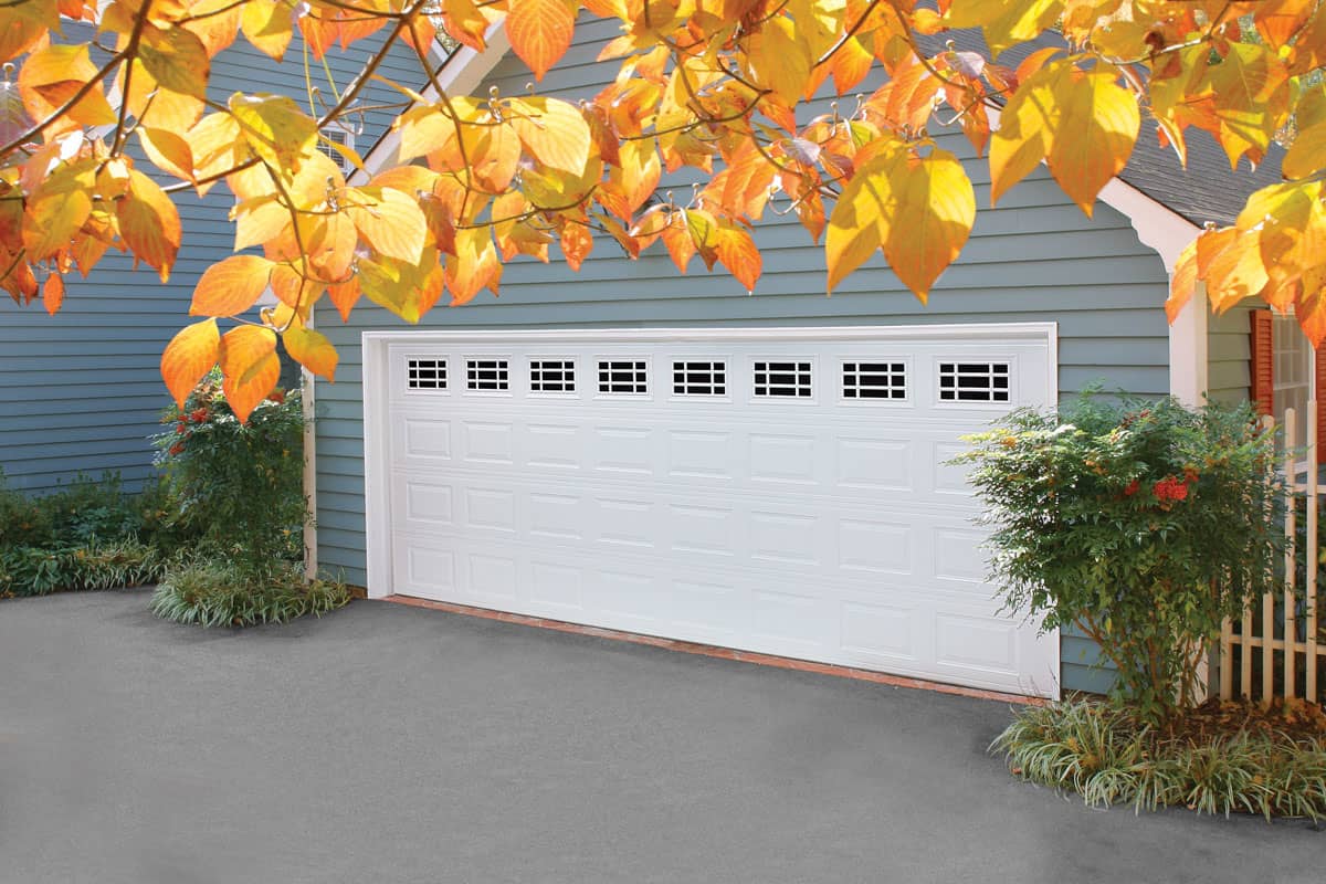 House with a steel garage door behind fall leaves